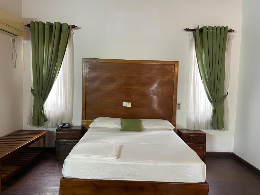 1 dormitorio con 1 cama grande y cortinas verdes en Hotel Neithal Batticaloa, en Batticaloa