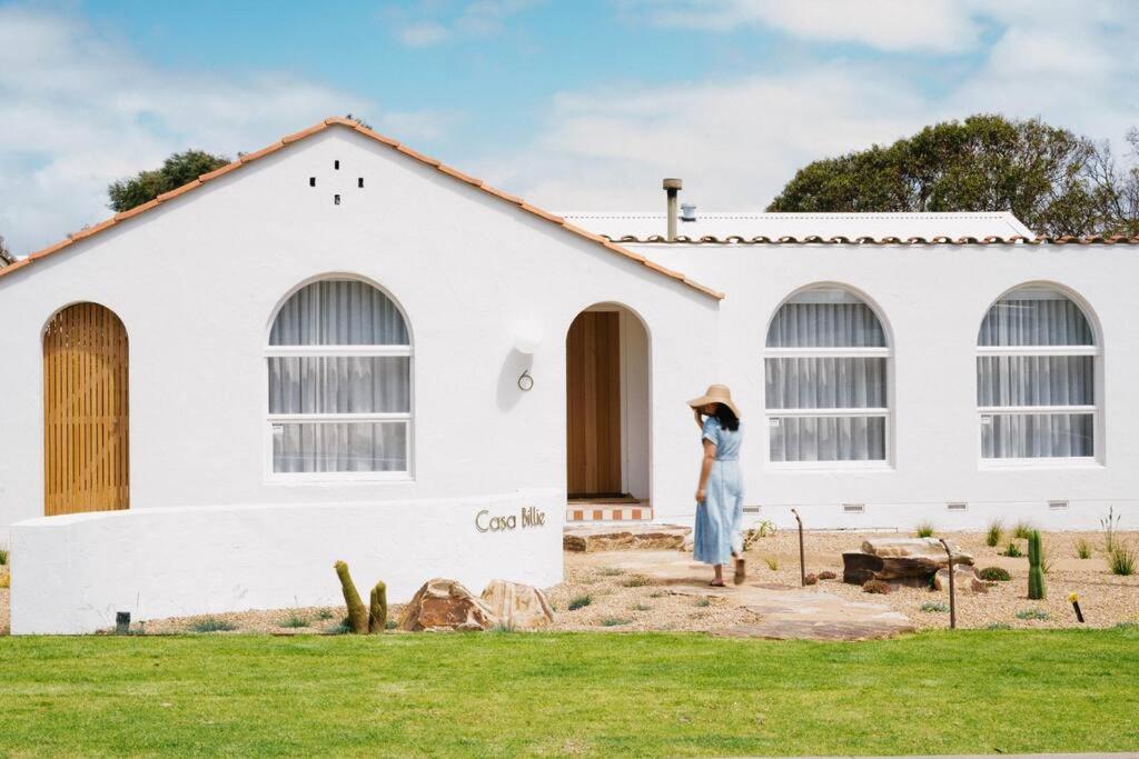 Una donna in piedi davanti a una casa bianca. di Casa Billie: Luxury stay 200m to pristine coastline a Aldinga Beach