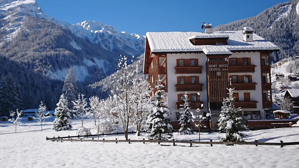 ein Gebäude im Schnee mit Bäumen und Bergen in der Unterkunft Sport Hotel Cristal in Falcade