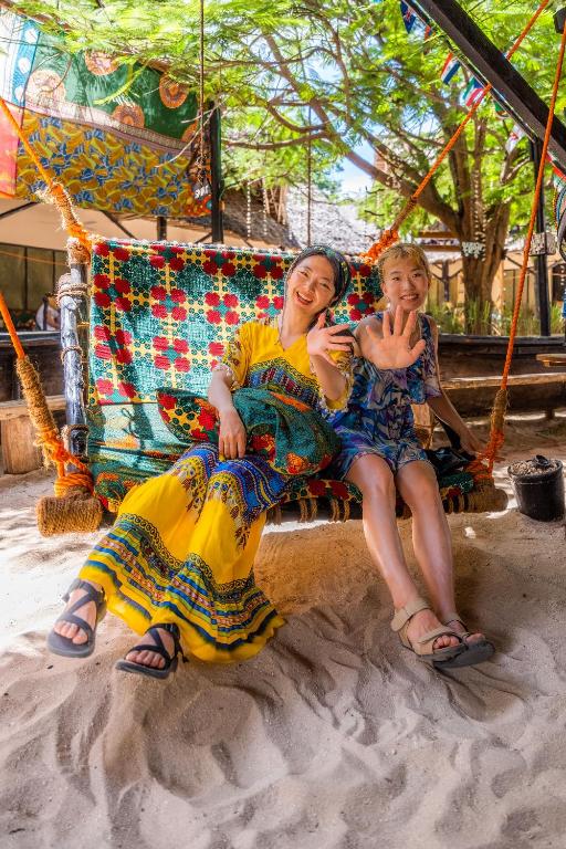two women sitting on a swing in the sand at Makofi Guest House in Nungwi