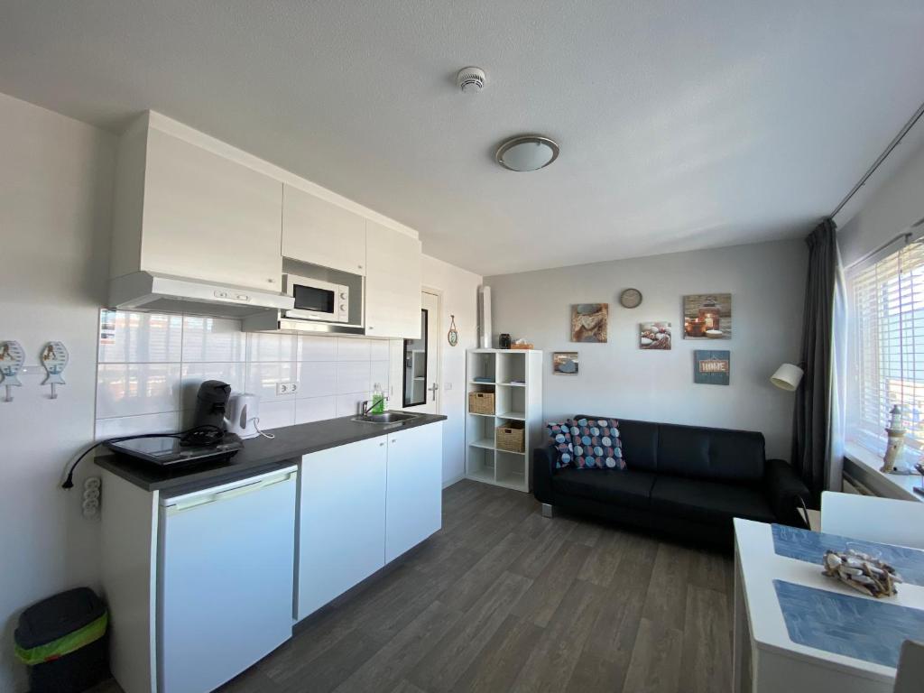 a kitchen and living room with white cabinets and a couch at Hollandse Nieuwe in Katwijk aan Zee