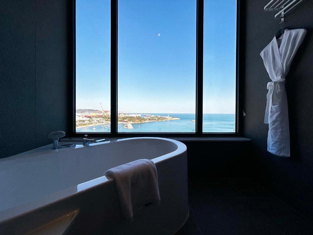 a bathroom with a tub and windows with a view of the ocean at Ulsan Tanibay Hotel & Wedding in Ulsan