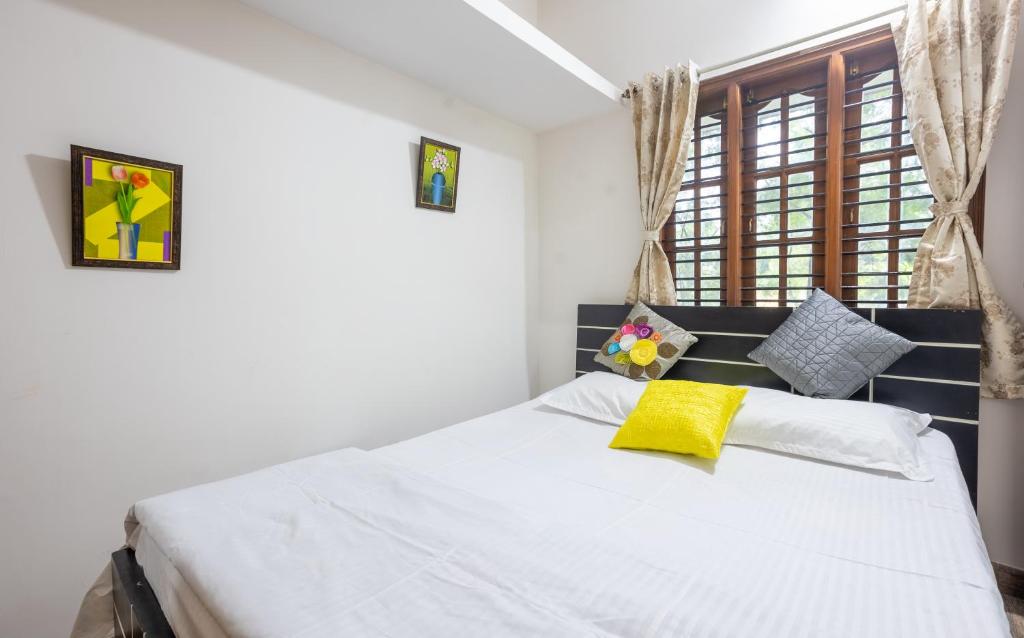 - une chambre avec un lit blanc et un oreiller jaune dans l'établissement Shree Miththam Apartment, à Bangalore