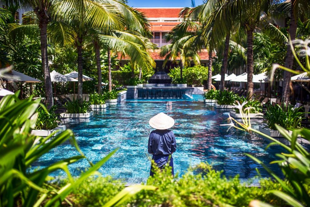 a person wearing a hat standing in front of a pool at Almanity Hoi An Resort & Spa in Hoi An