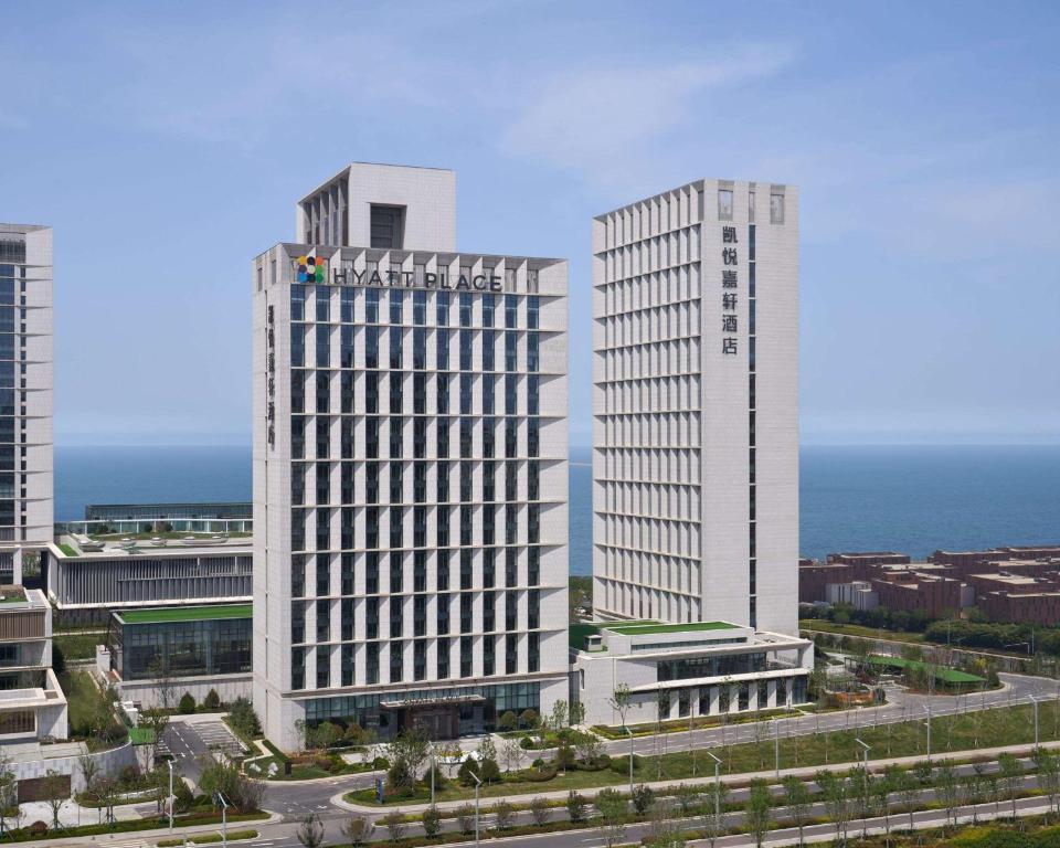 two tall white buildings in front of the ocean at Hyatt Place Yantai Development Zone in Yantai