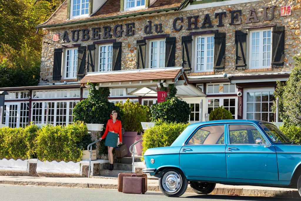 una mujer parada frente a un edificio con un coche azul en L’Auberge du Château en Dampierre