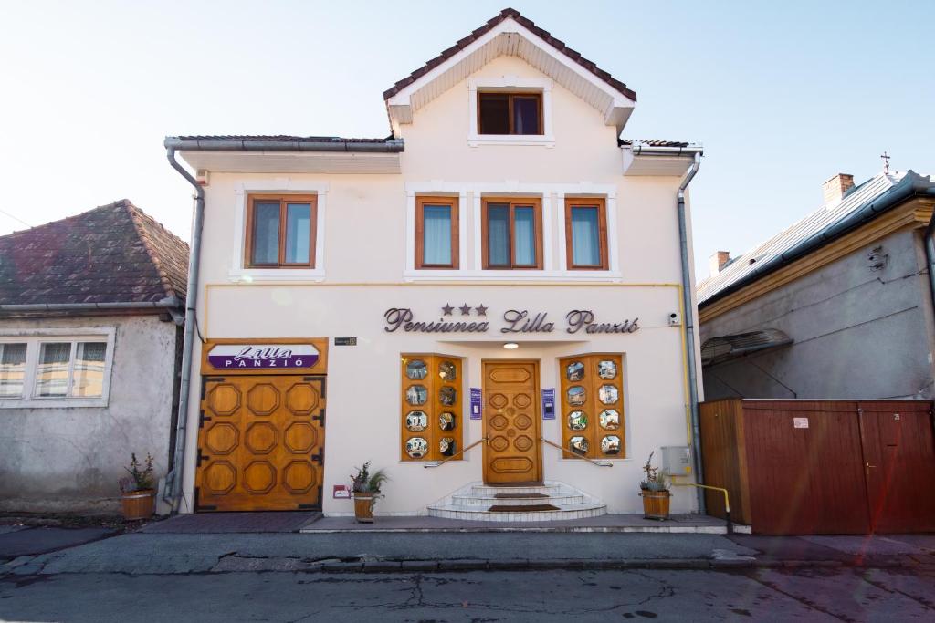 a white building with brown doors on a street at Lilla Panzió in Odorheiu Secuiesc