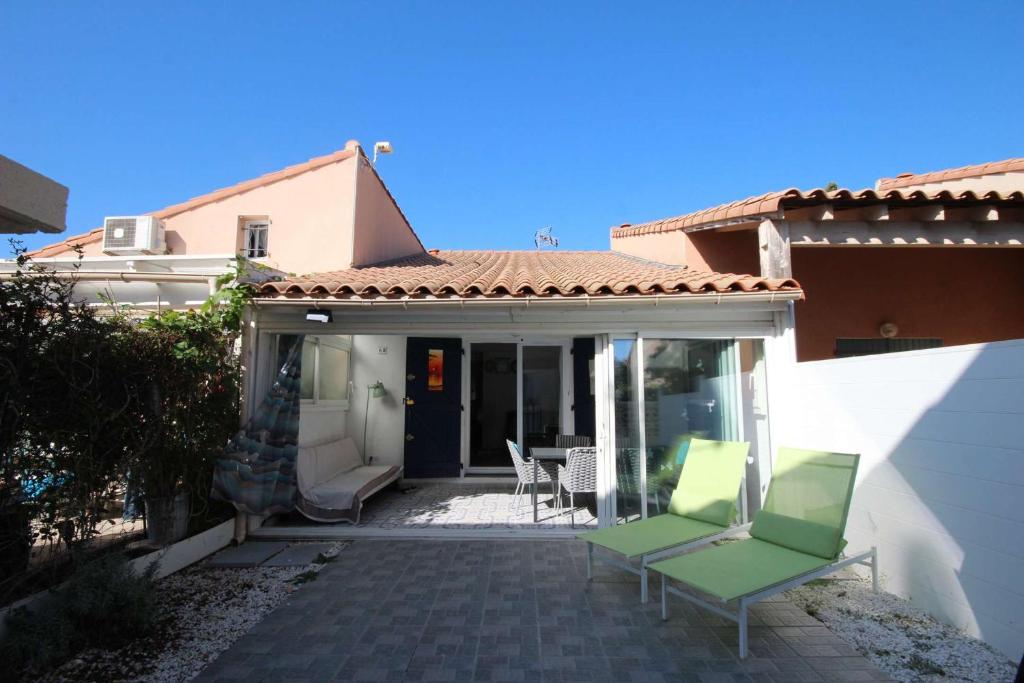 une terrasse avec 2 chaises vertes et une maison dans l'établissement Jolie Maison T3 mezzanine climatisée avec veranda, 4 à 5 couchages, terrasse clôturée, WIFI inclus, Résidence LES MARINES, 200m de la plage LRMA68B, à Portiragnes