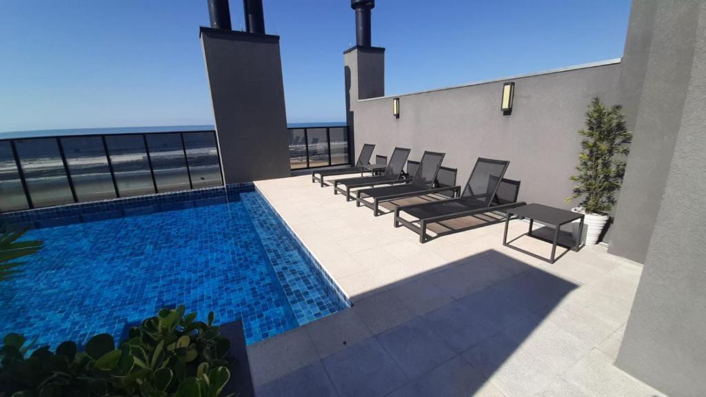 une piscine avec des chaises et l'océan en arrière-plan dans l'établissement Studio 110 Maravilhoso Vista Mar Piscina Aquecida, à Matinhos