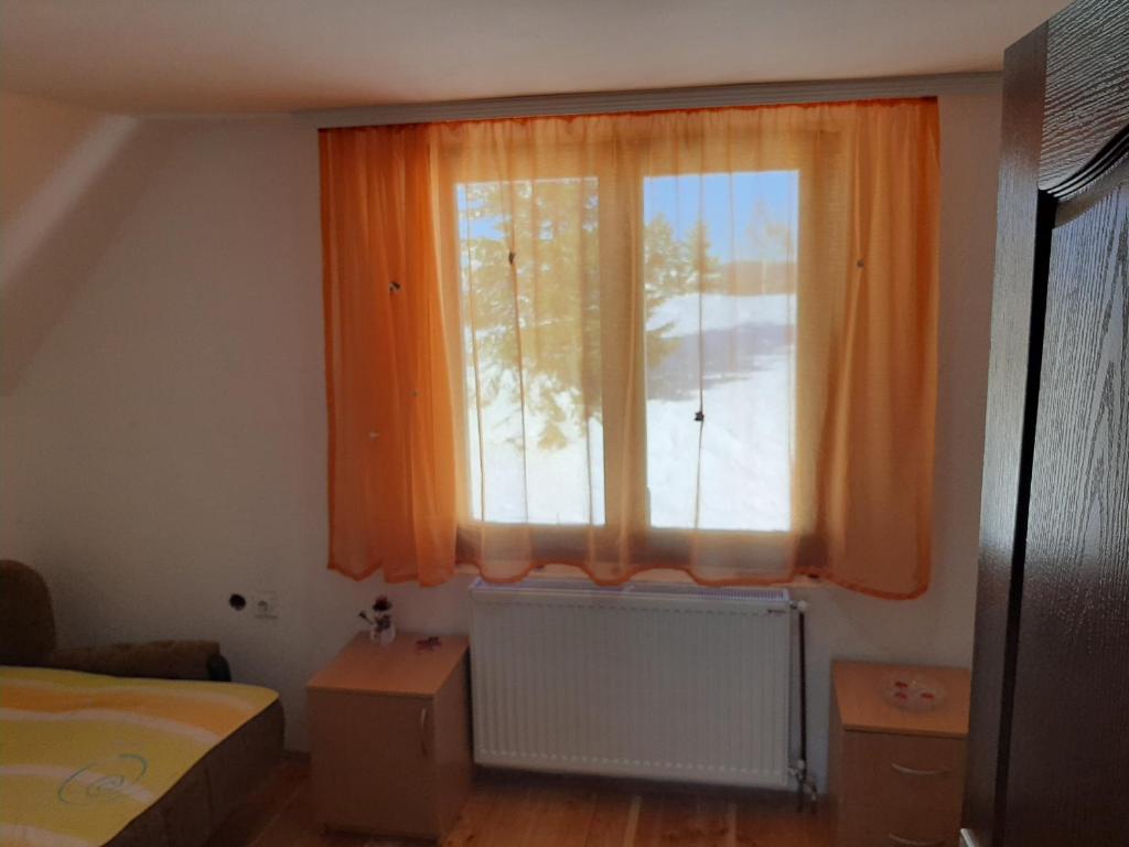 1 dormitorio con ventana y cortina naranja en Vikend kuća Vukašinović, en Kopaonik