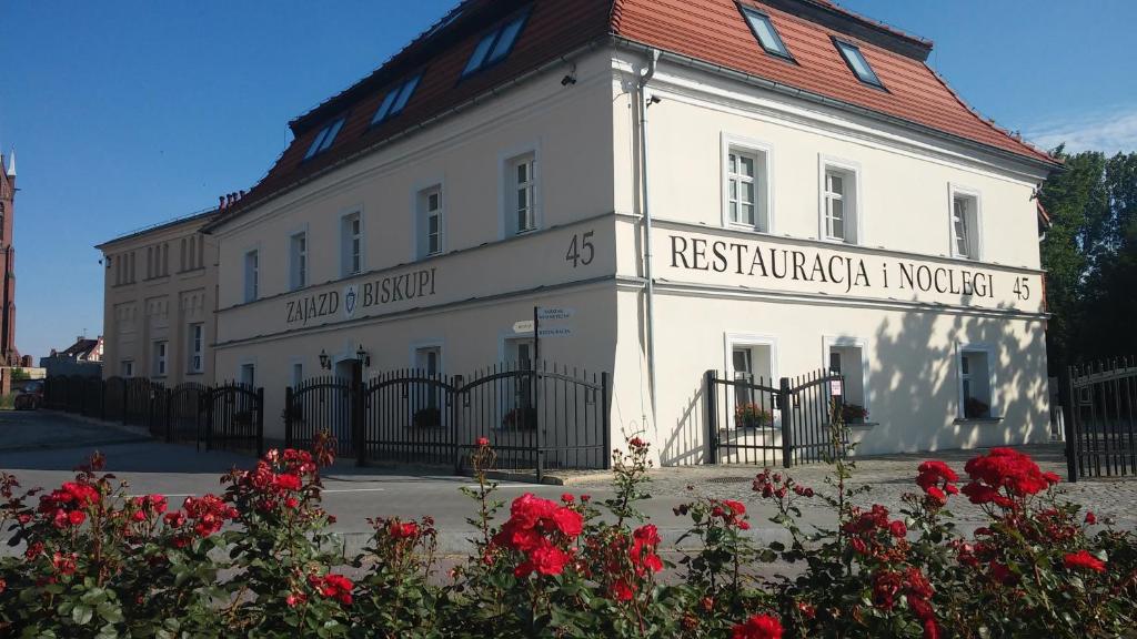 a white building with a red roof and red flowers at Zajazd Biskupi in Racibórz