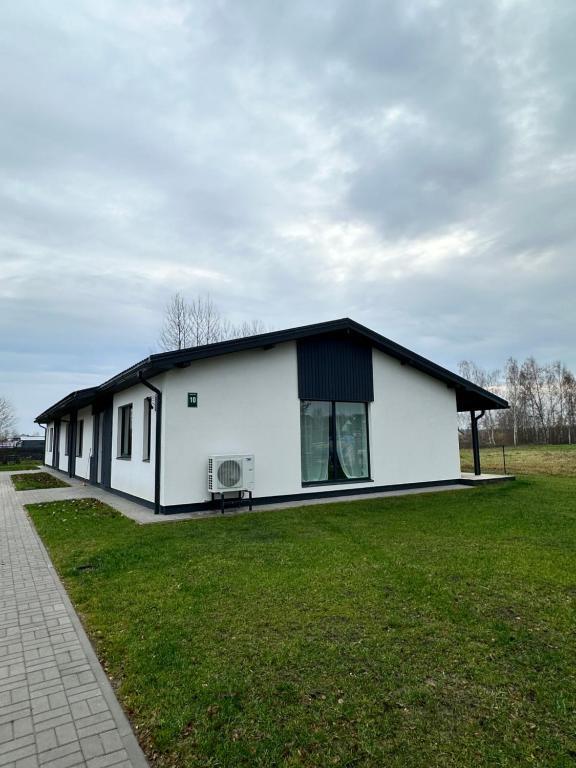 a white building with a black roof on a grass field at Marupe Saules in Mārupe