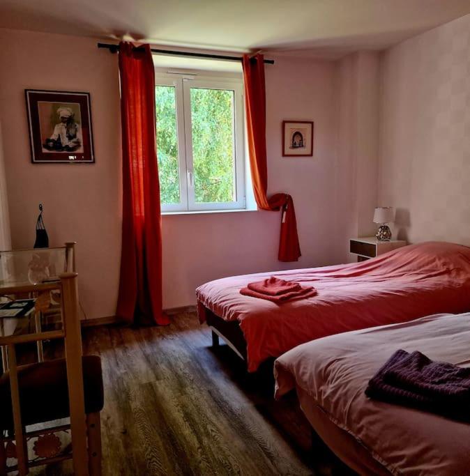 a bedroom with two beds and a window with red curtains at La Maison Thébaïde in Mortagne