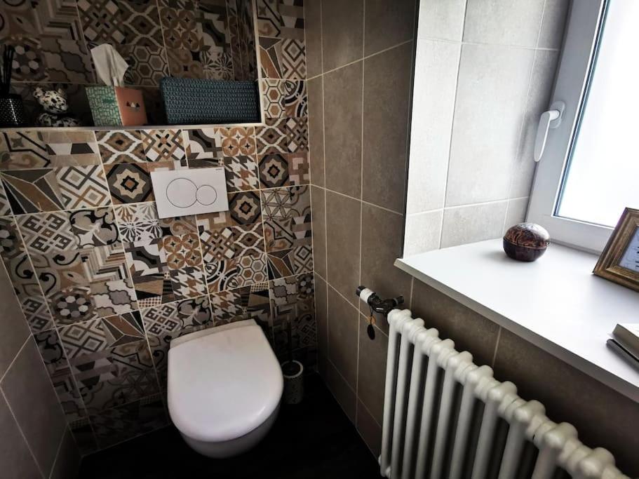 a bathroom with a toilet and a tile wall at La Maison Thébaïde in Mortagne