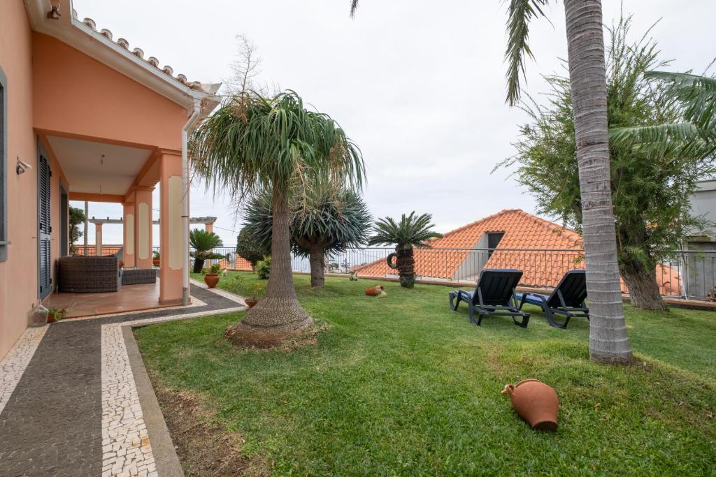 a yard with palm trees and chairs and a house at Sara House in Ponta do Sol