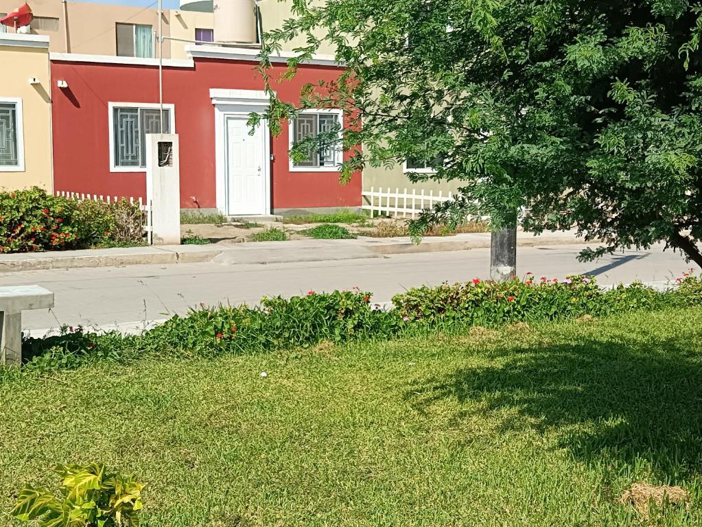 un edificio rojo con un árbol frente a una calle en CASA CON COCHERA CERCA A LA PLAYA PlMENTEL en Chiclayo