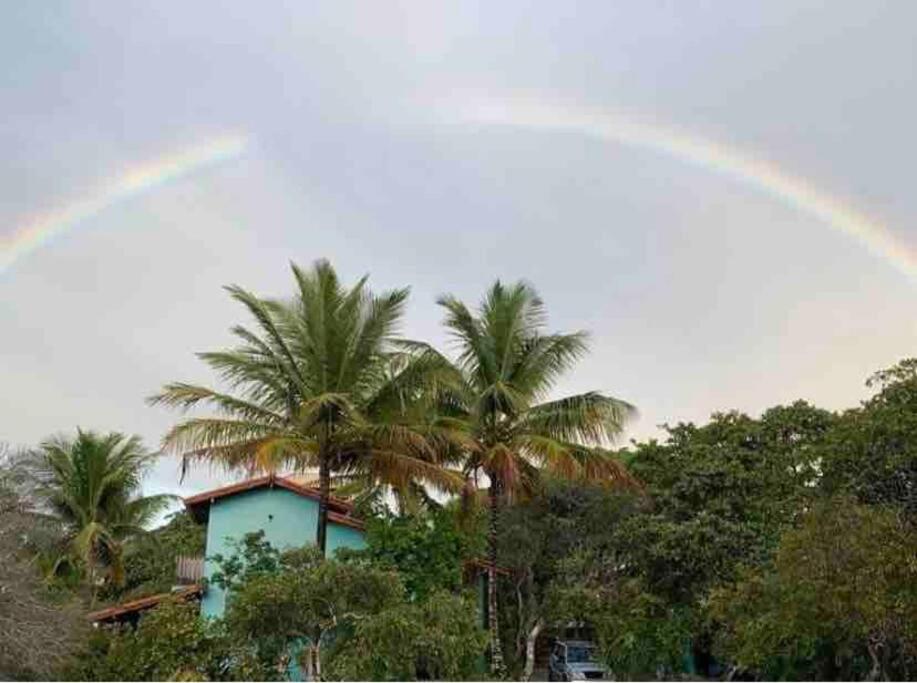 een regenboog boven een blauw huis met palmbomen bij Recanto das Cigarras in Cumuruxatiba
