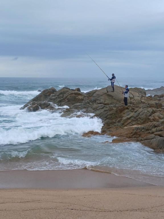 two people are fishing on rocks on the beach at Ocean Splendour in Uvongo Beach
