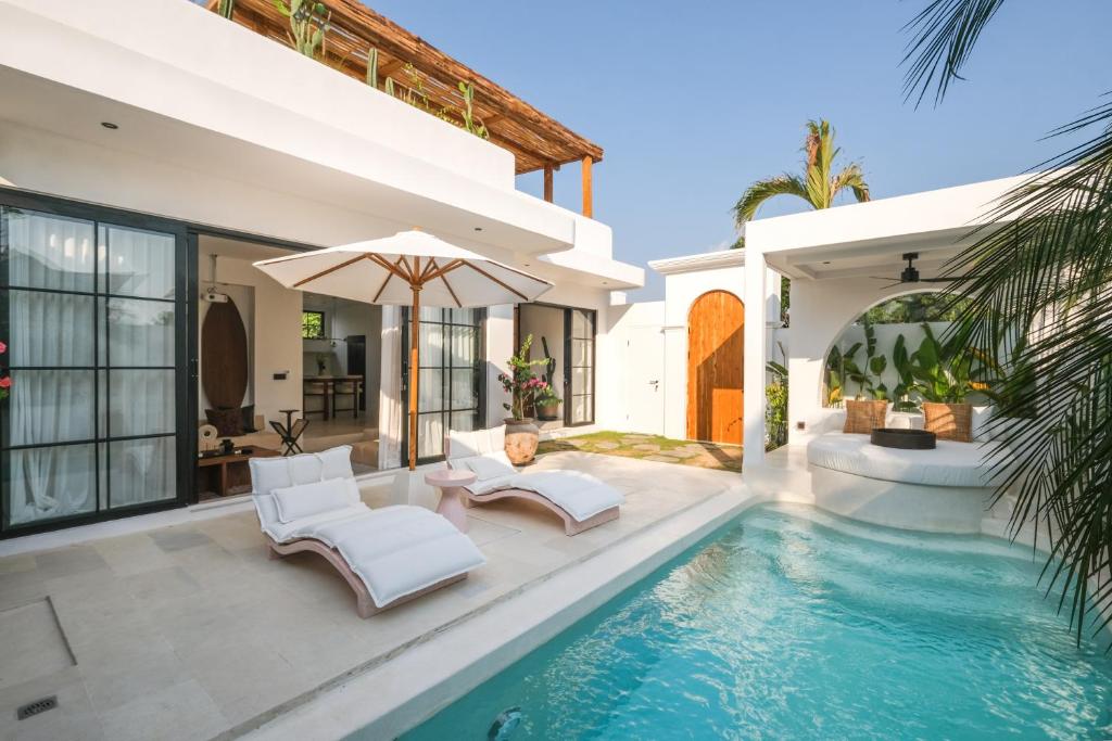 a villa with a swimming pool with two chairs and an umbrella at Villa Sama Canggu in Canggu