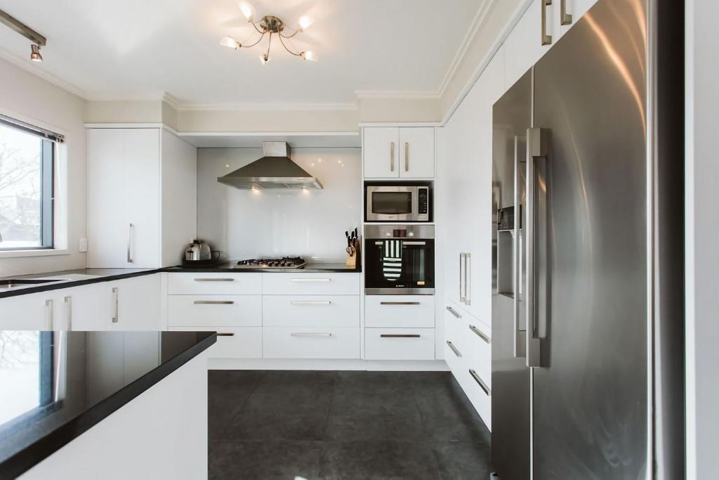 a kitchen with white cabinets and a stainless steel refrigerator at Seven By The Sea Tourist Hot Spot in New Plymouth