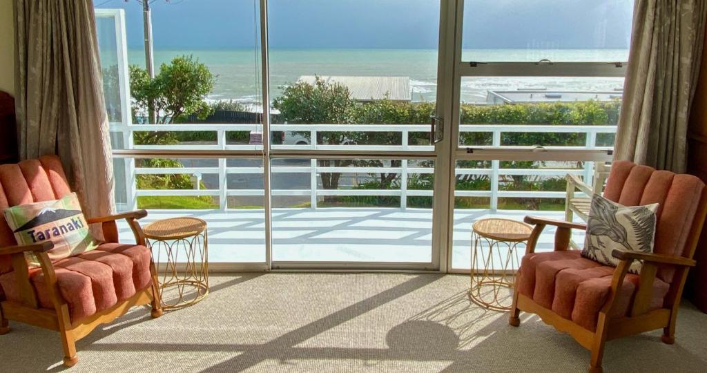 Habitación con 2 sillas y vistas al océano. en Messenger Magic A Classic Kiwi Bach, en Oakura