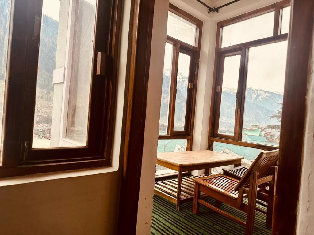 een tafel en stoelen in een kamer met ramen bij Hotel Alpine in Manāli