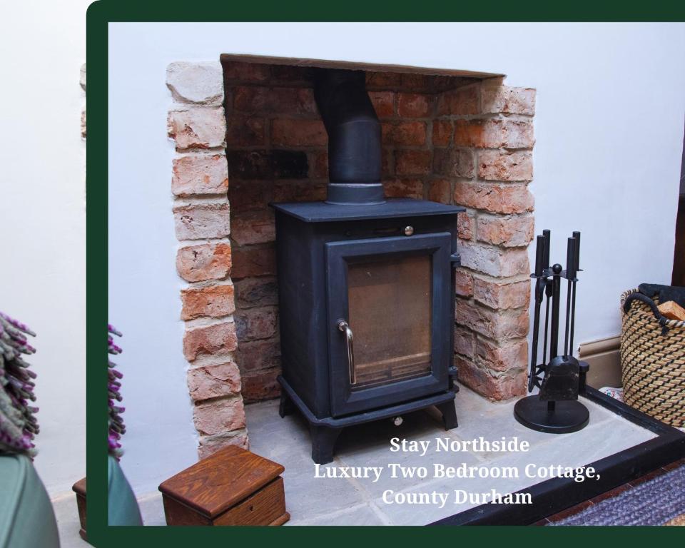 a black stove in a room with a brick wall at Stay Northside - Log Burner, Luxury Countryside Cottage County Durham 