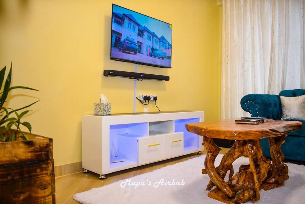 sala de estar con mesa y TV en la pared en Mupa's Luxury Condo II, en Nyahururu