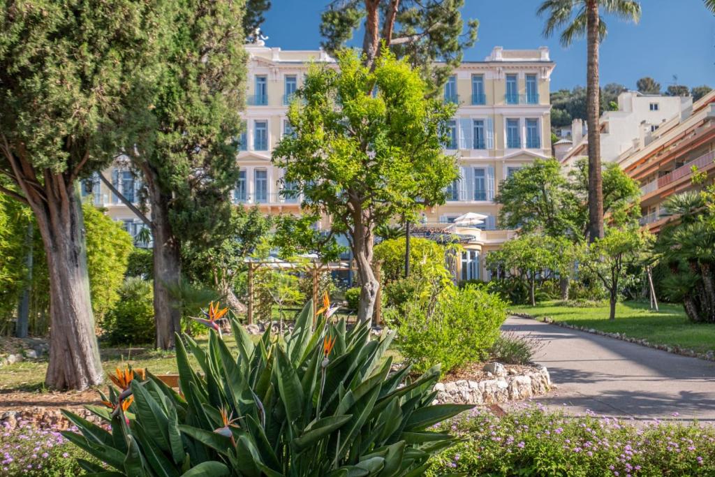 a building in a park with trees and flowers at Hôtel Miléade L'Orangeraie - Menton in Menton