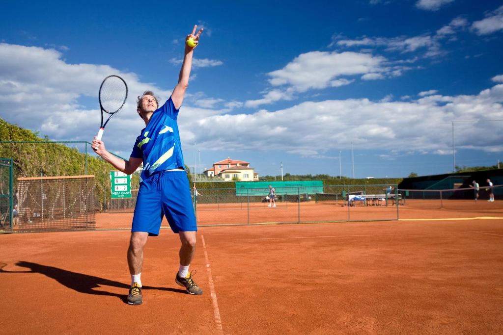 a man holding a tennis ball and racket on a tennis court at Valamar Diamant Hotel in Poreč
