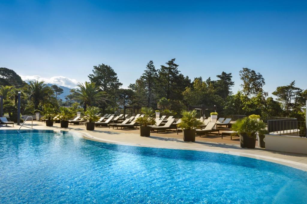 a pool at a hotel with lounge chairs and mountains at Imperial Valamar Collection Hotel in Rab