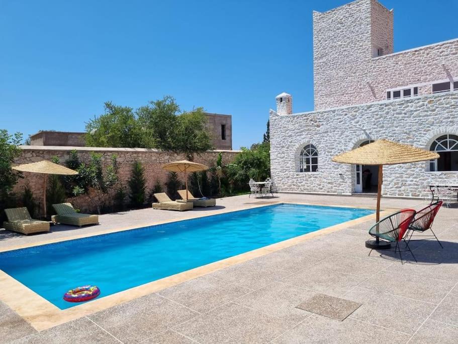 a swimming pool with chairs and umbrellas next to a building at Villa Les jardins fleuris in Essaouira