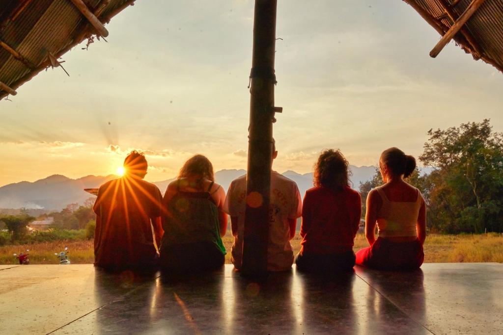 Eine Gruppe von Menschen, die auf einer Veranda sitzen und den Sonnenuntergang beobachten. in der Unterkunft Cody Backpackers in Pai