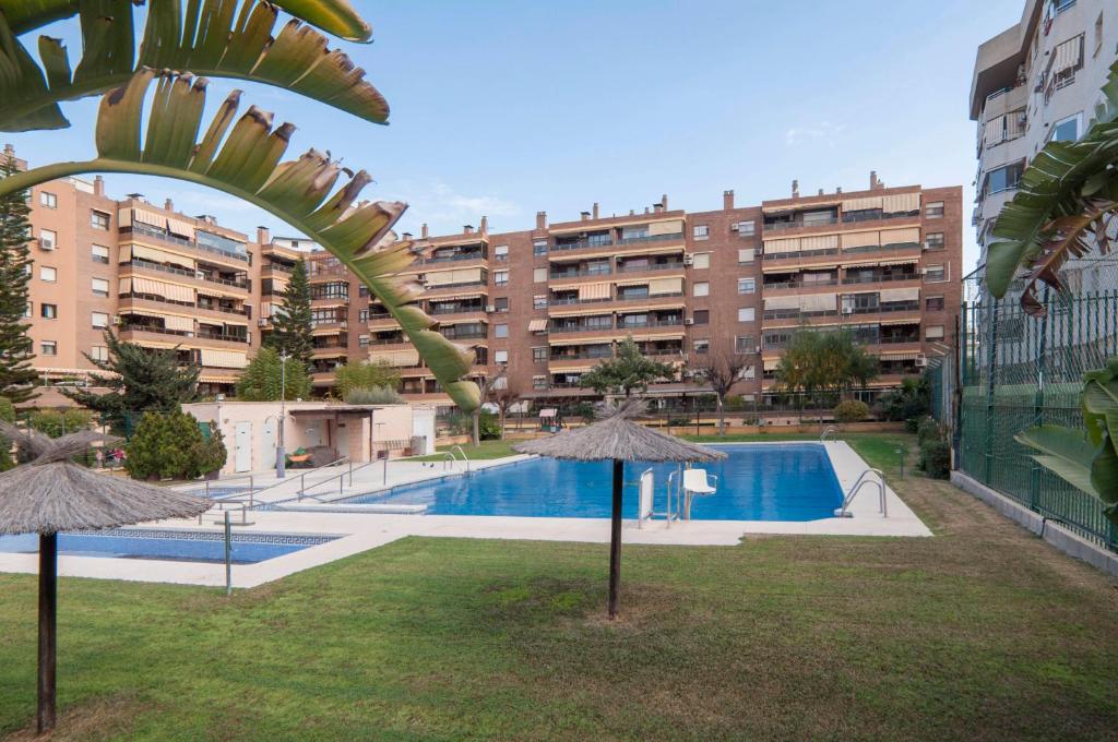 una piscina con 2 sombrillas y un edificio en Málaga Capital - Zona Oeste: Parking-Wifi-Piscina en Málaga