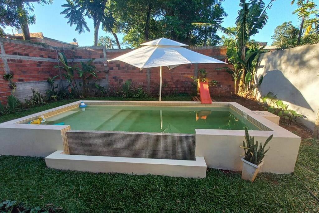 uma pequena piscina com um guarda-sol e uma parede de tijolos em Casa Laurel em Puerto Iguazú