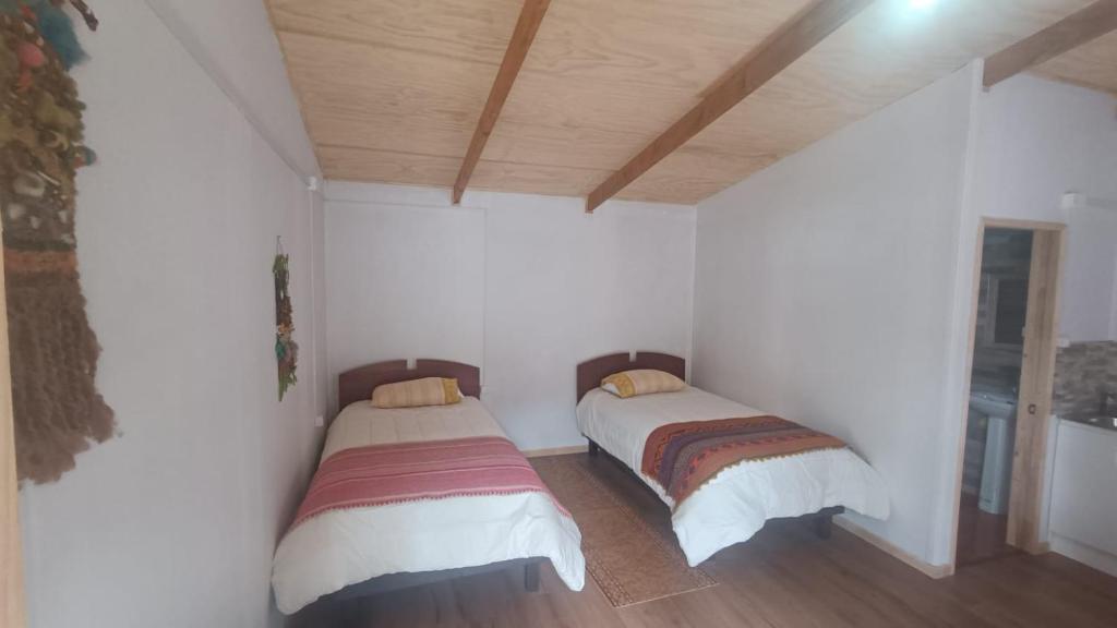 two beds in a room with white walls and wooden ceilings at Cerro Nevado in Puerto Tranquilo