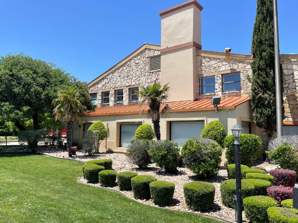 a house with bushes and trees in front of it at Studio 6 Suites North Richland Hills TX in North Richland Hills