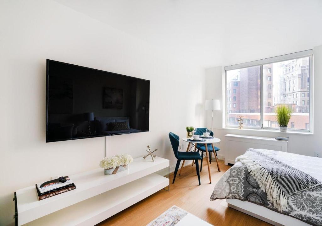 - une chambre blanche avec une grande télévision murale à écran plat dans l'établissement Modern Studio Apartment At East Side, à New York