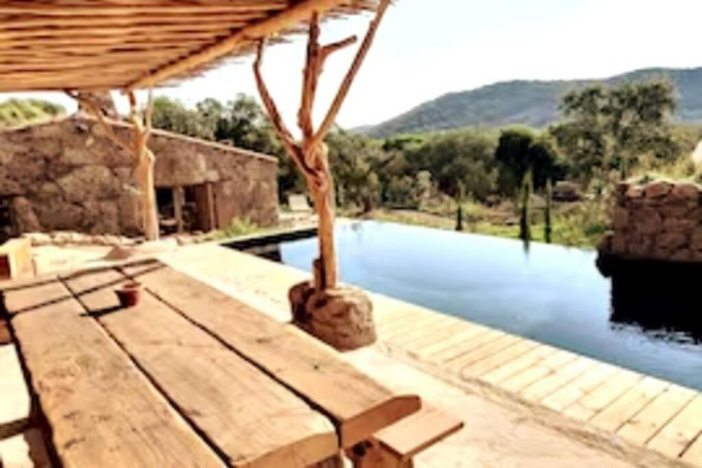 - une piscine avec une table en bois à côté d'une rivière dans l'établissement Bergerie #Casa di Petra à Palombaggia avec piscine, à Porto-Vecchio
