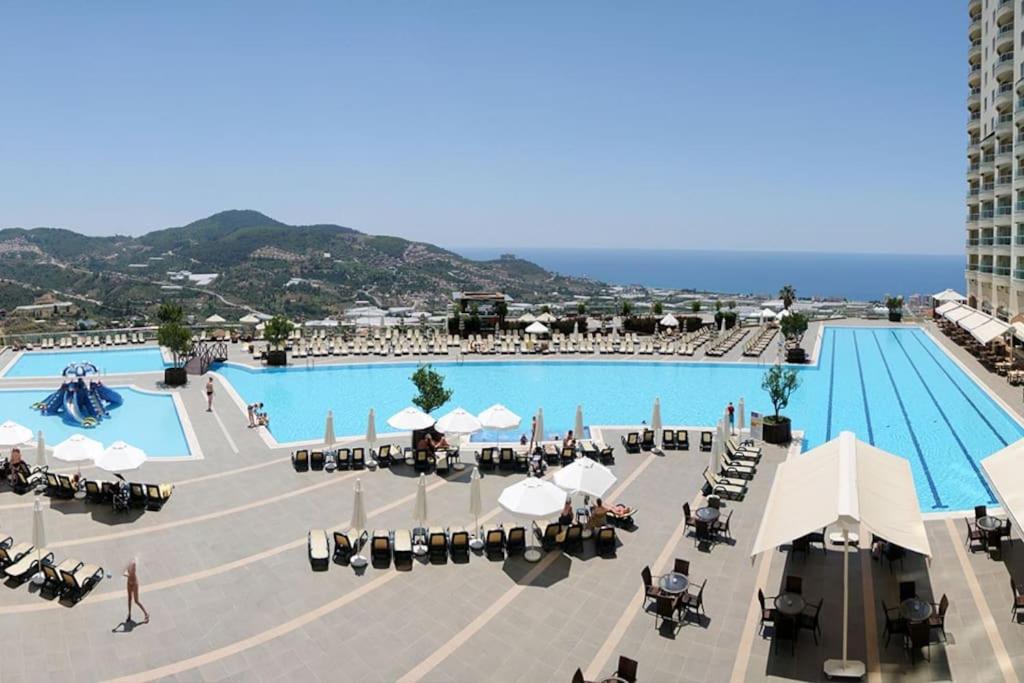 una gran piscina con mesas y sillas junto a un edificio en Gold City 5 star resort 2+1 appartement sea view and aqua park, en Alanya