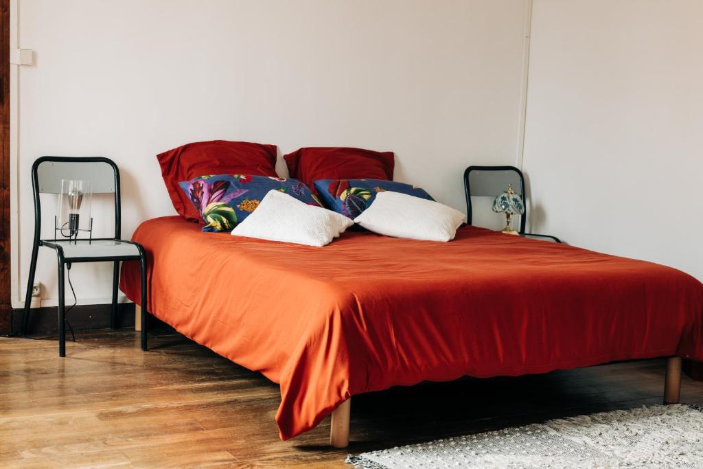 a bed with an orange blanket and pillows on it at La Maison de Laulie in Bagnères-de-Bigorre