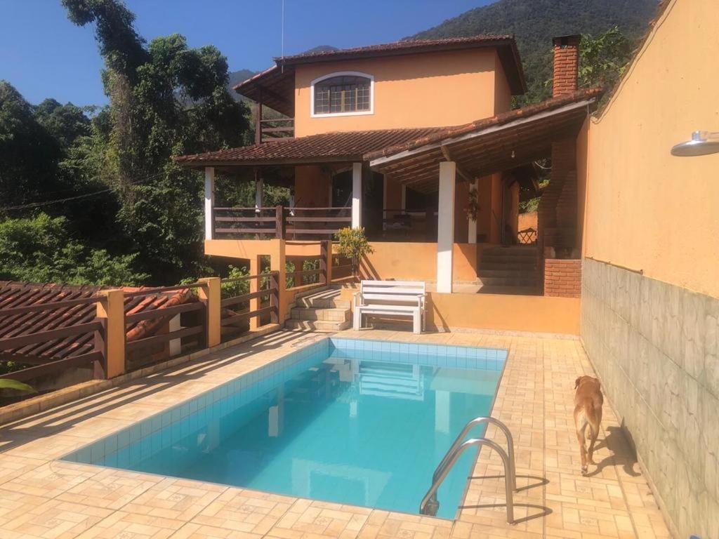 a dog standing next to a swimming pool in front of a house at Pousada e Hostel Casa da Jura in Ilhabela