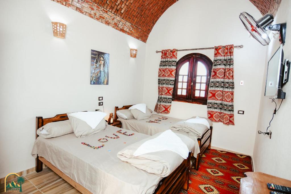 amzran hotel siwa في سيوة: سريرين في غرفة بجدران بيضاء وتلفزيون