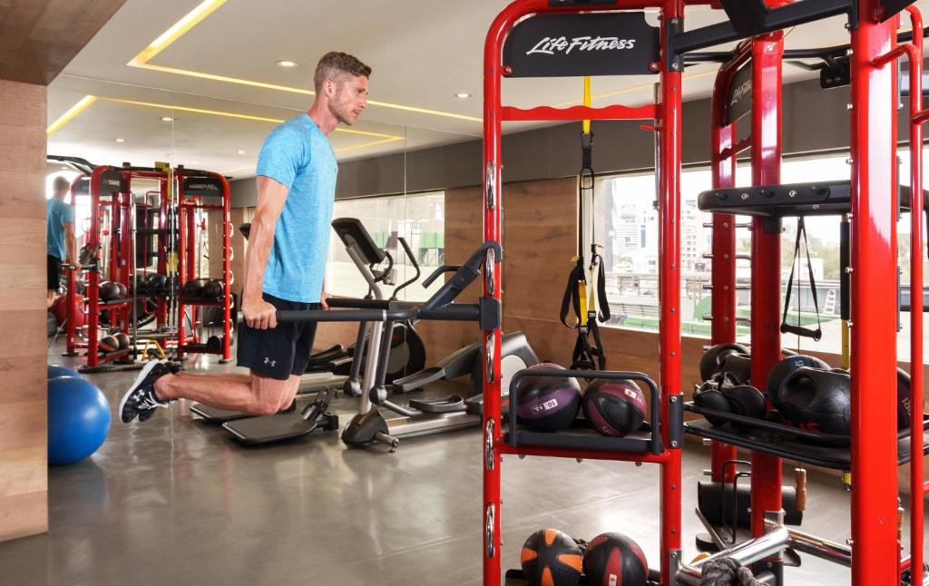 A guest using a red functional-training machine in a mirrored hotel gym.