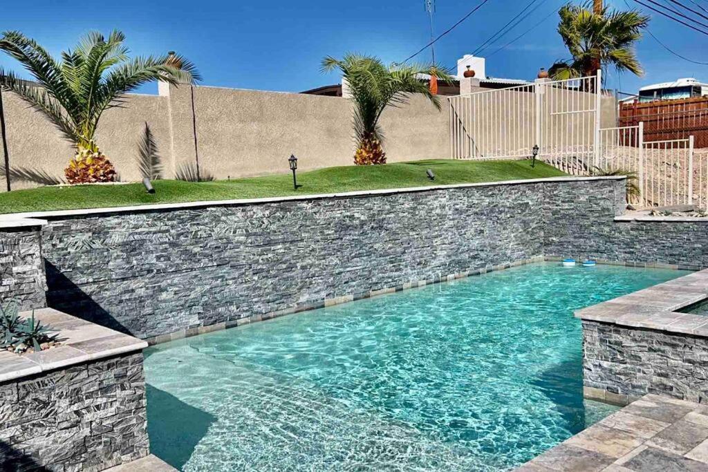 a swimming pool with a brick retaining wall and palm trees at Paradise Oasis! Waterfall pool & spa in Lake Havasu City