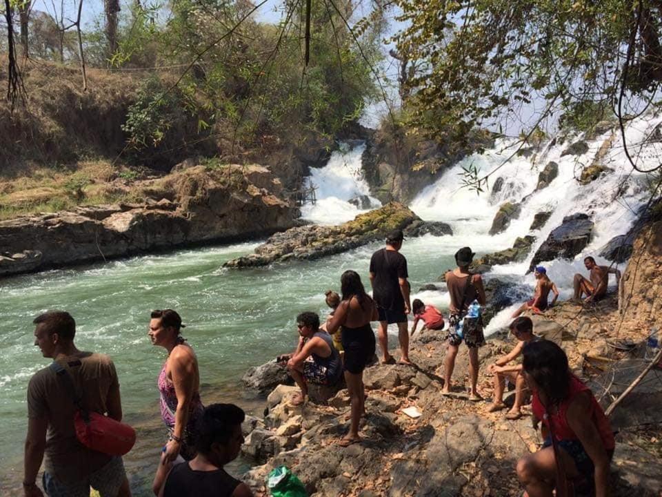 un grupo de personas de pie en las rocas cerca de un río en Dondet guesthouse, en Muang Không