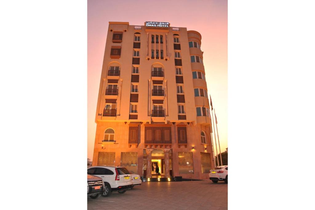 een hoog gebouw met auto's geparkeerd voor het bij Capital O 155 Dmas Hotel in Muscat