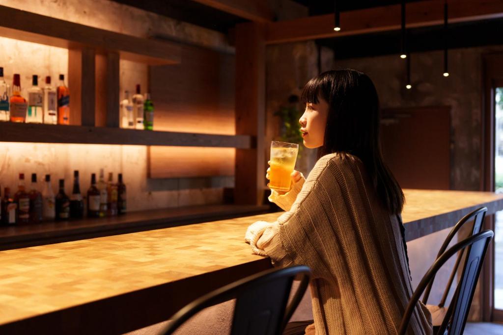 Eine Frau, die an einer Bar sitzt und ein Glas hält. in der Unterkunft 3U NAMBA MINAMI by DOYANEN in Osaka