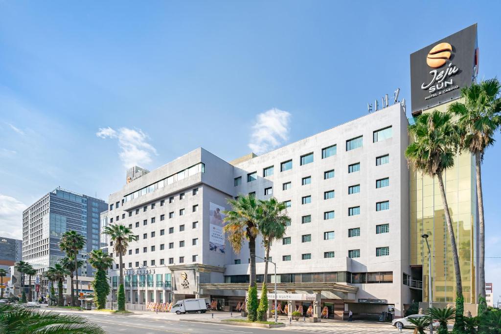 a large white building with palm trees in front of it at Jeju Sun Hotel & Casino in Jeju