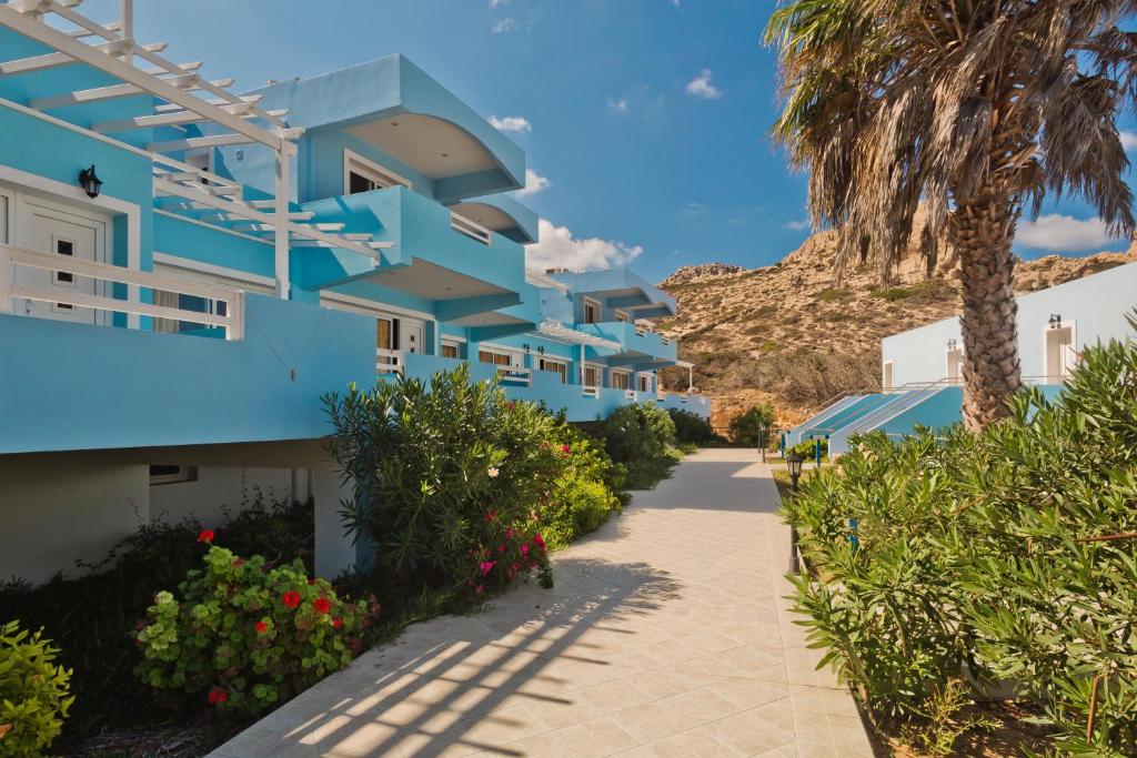 a blue building with a palm tree and a sidewalk at Royal Beach Hotel in Arkasa